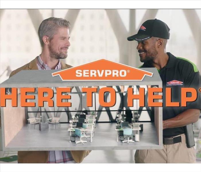 Two SERVPRO employees looking at each other behind a picture of desk in a building 